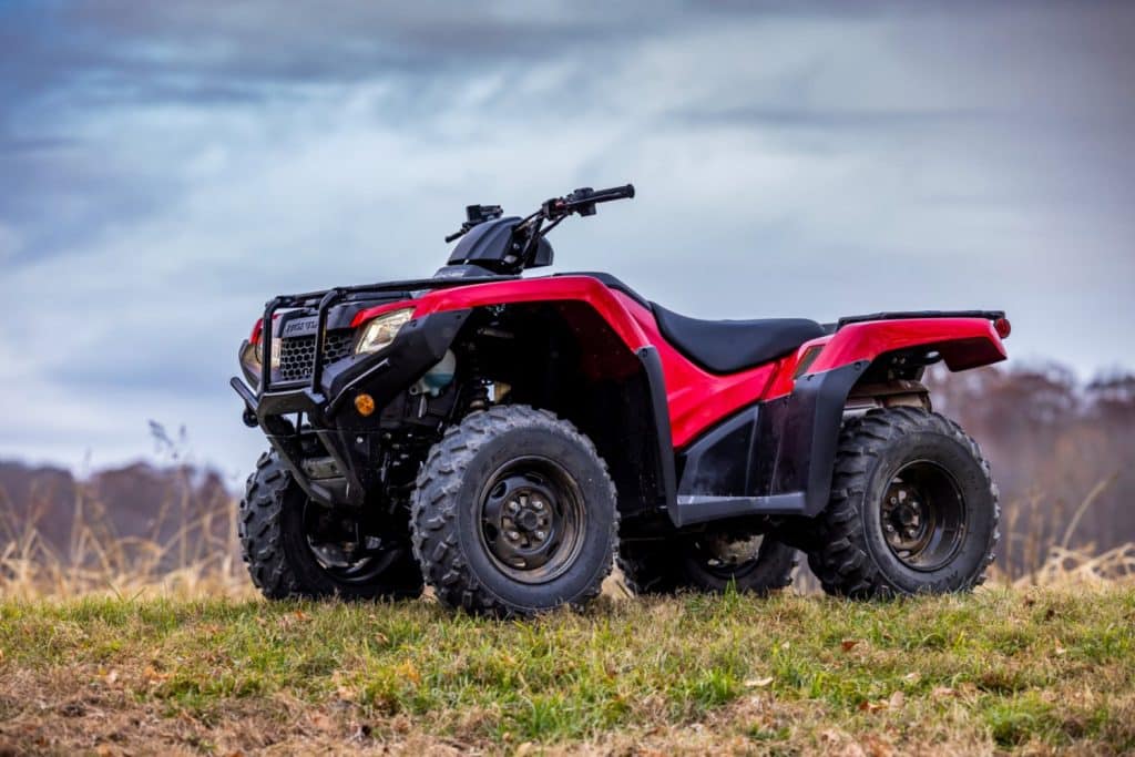 A high-resolution shot of the 2026 Honda FourTrax Rancher navigating muddy terrain at sunrise.