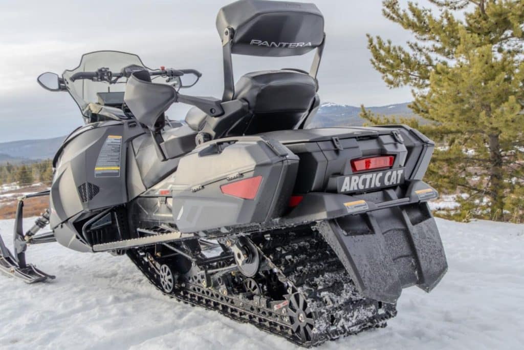 Rear three-quarter view of an Arctic Cat Pantera touring snowmobile with passenger backrest, side storage cases, mirrors, and cargo box parked on snowy mountain terrain.